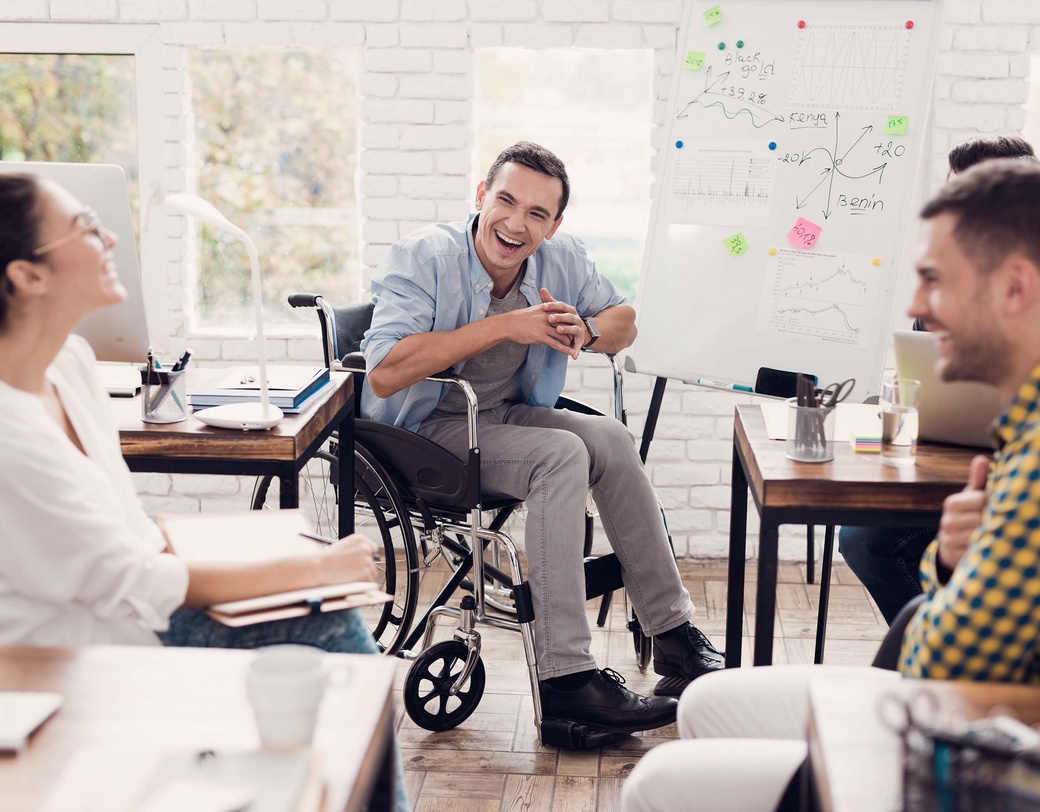 Group of employees having a happy conversation around a white board, one employee in a wheelchair.