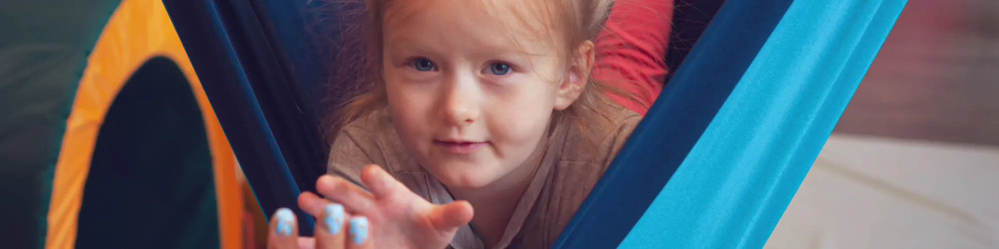 Little girl sitting in hammock reaching out to touch a volunteer's hand.