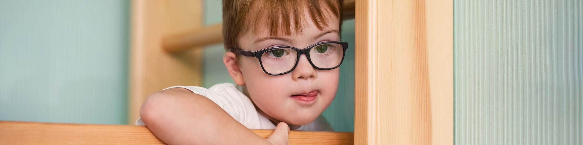 Child with glasses and white shirt on wooden ladder.