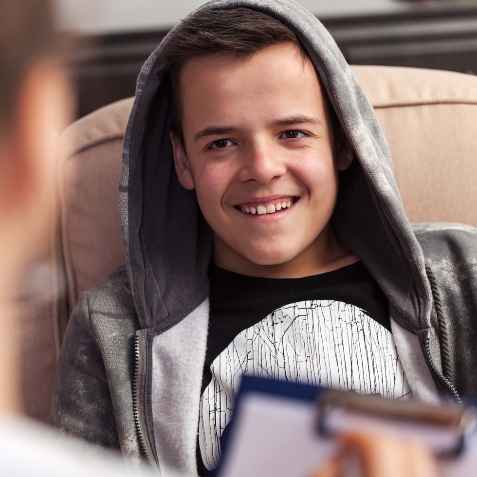 Child with hood over head smiling while speaking with healthcare professional.