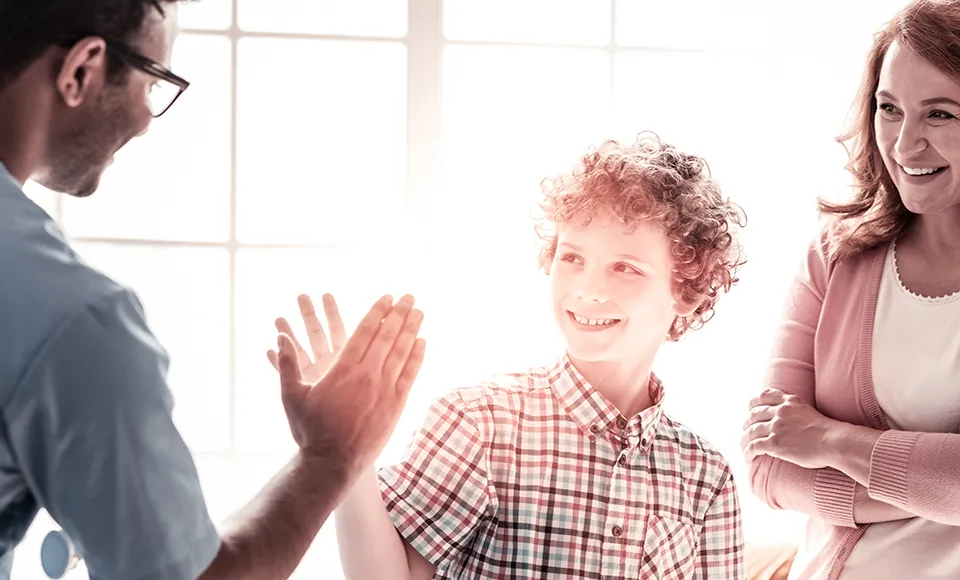 Clinician giving a boy a high-five while his mom smiles