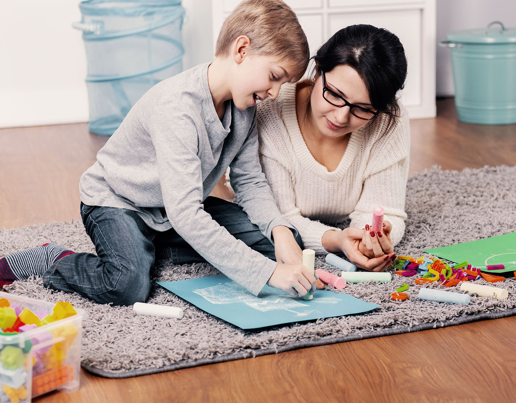 Parent and child creating chalk art while on a rug on the floor. 
