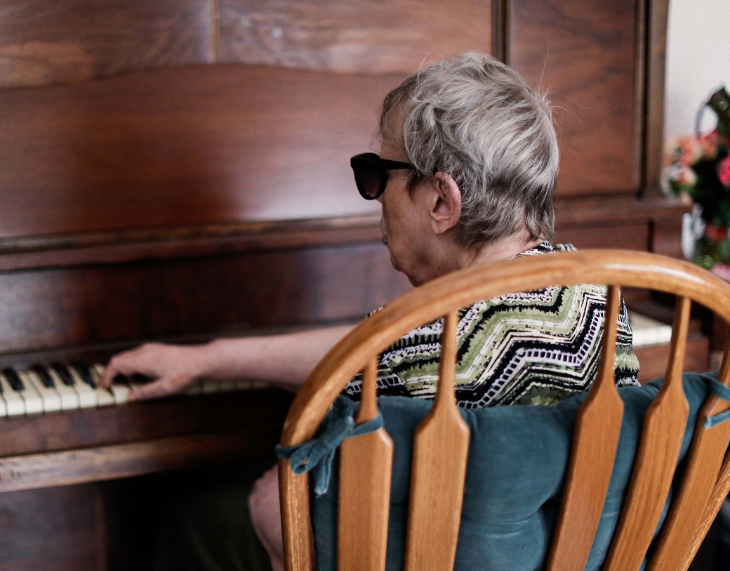 Senior person with sunglasses on, sitting at piano.