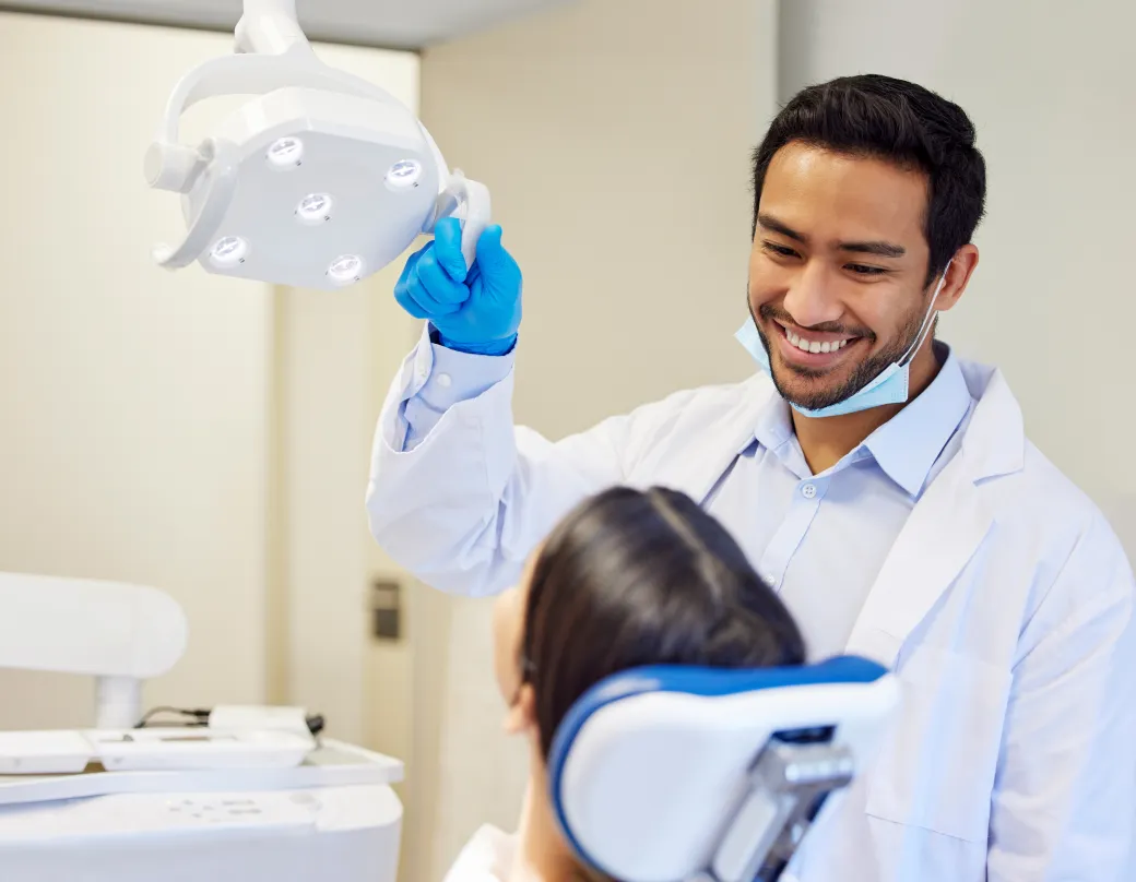 A dentist adjusting an examining light at a dentist office with patient in a chair 