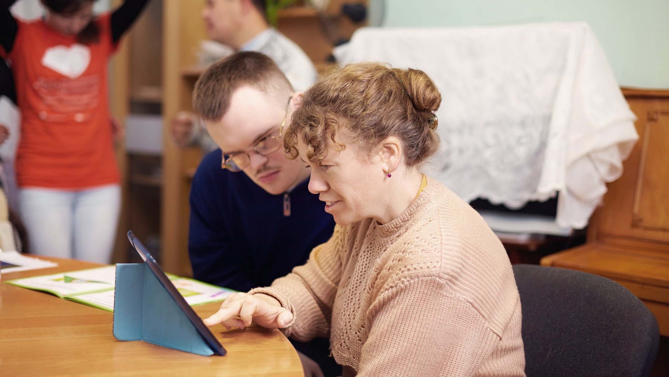 Care provider sitting at table with patient, looking at tablet.