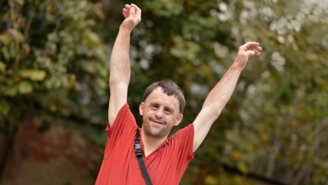 Adult outside, smiling with arms in the air.