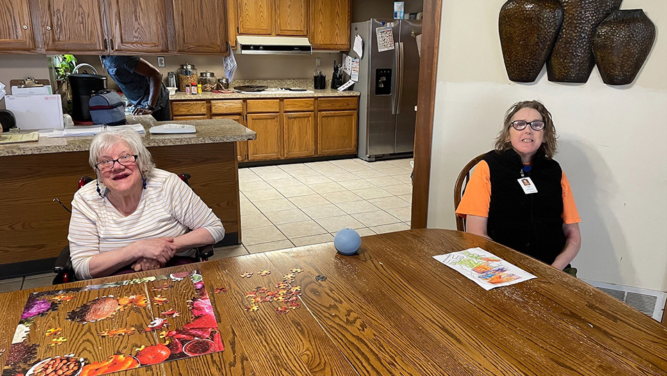 Resident and Boundless employee work on a puzzle next to an Echo Dot