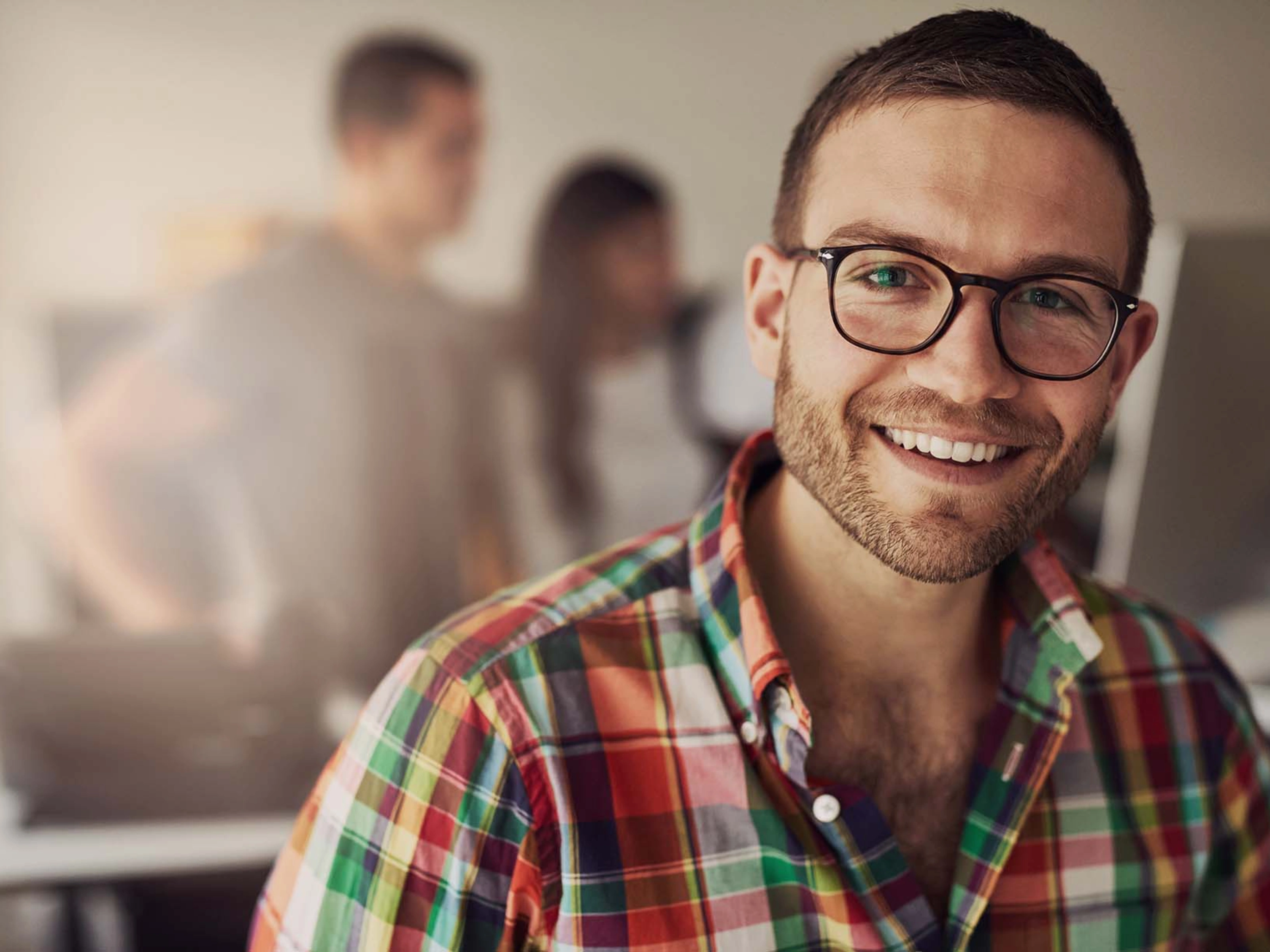 Person smiling at camera in office setting, people in the background.