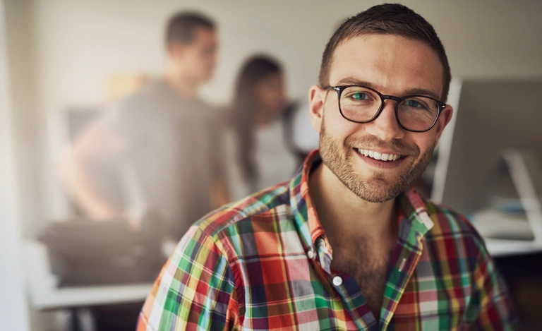 Person smiling at camera in office setting, people in the background.