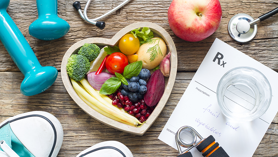 Fruit in a heart-shaped bowl surrounded by prescription pads, medical, and fitness equipment