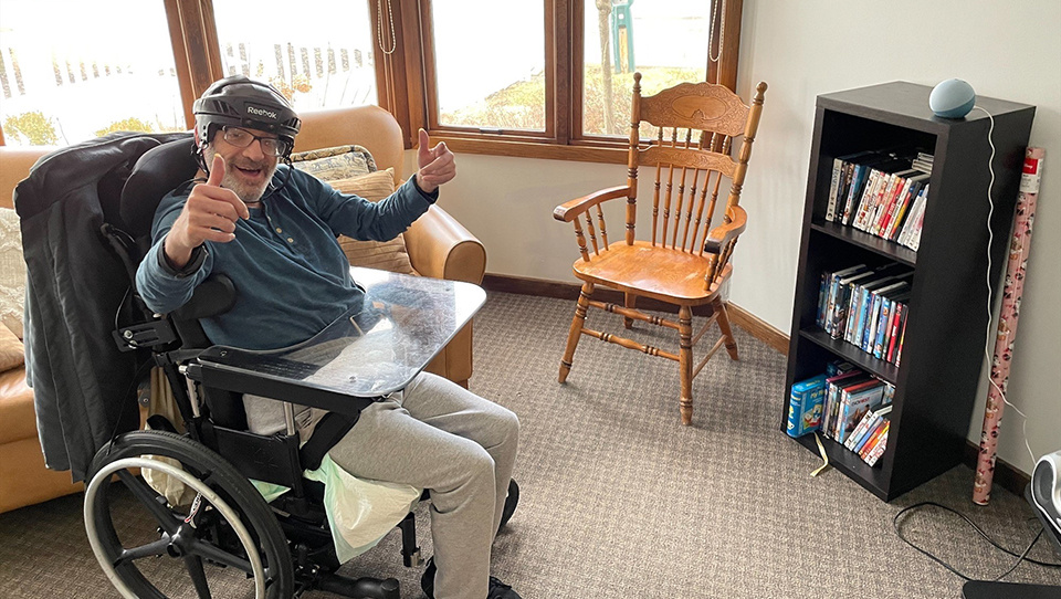Man in a wheelchair in a room with an echo dot giving a thumbs up