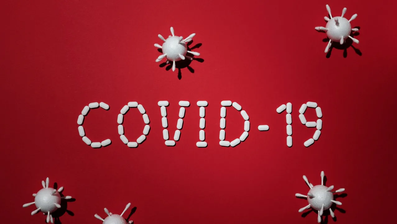 The word COVID-19 on a red background surrounded by images of a virus