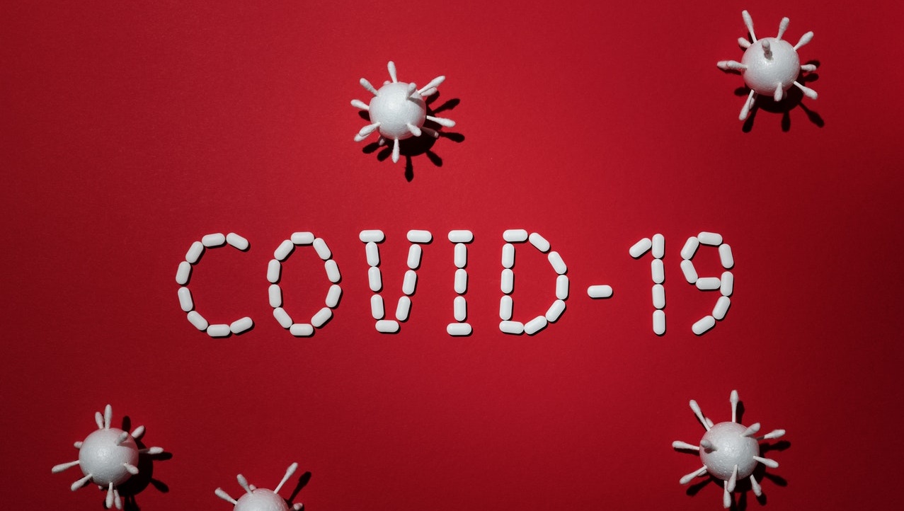 The word COVID-19 on a red background surrounded by images of a virus