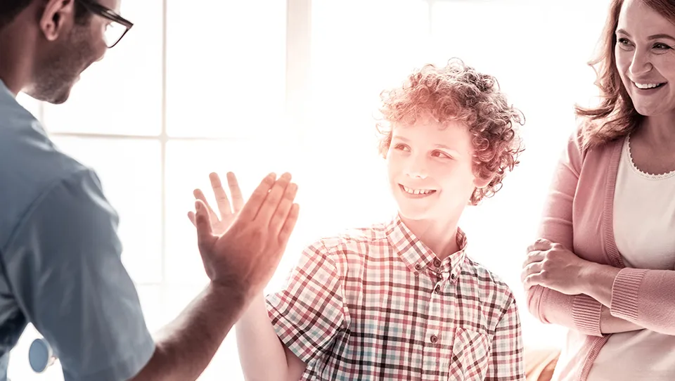 Counselor giving a young boy a high five while his mom watches
