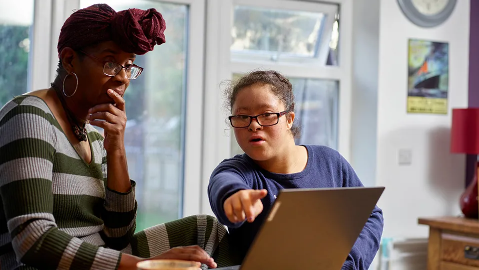 Woman and younger woman with  Down Syndrome using laptop at home 
