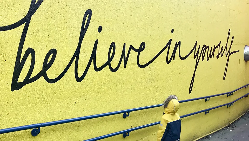 Young child looking at a wall that reads beliver in yourself. 