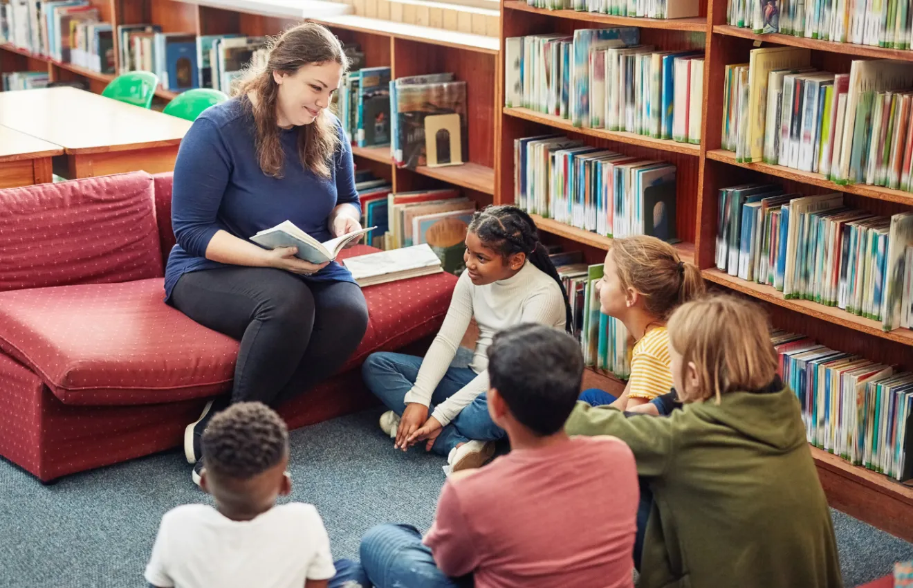 Adult seated reading a book to kids in a library