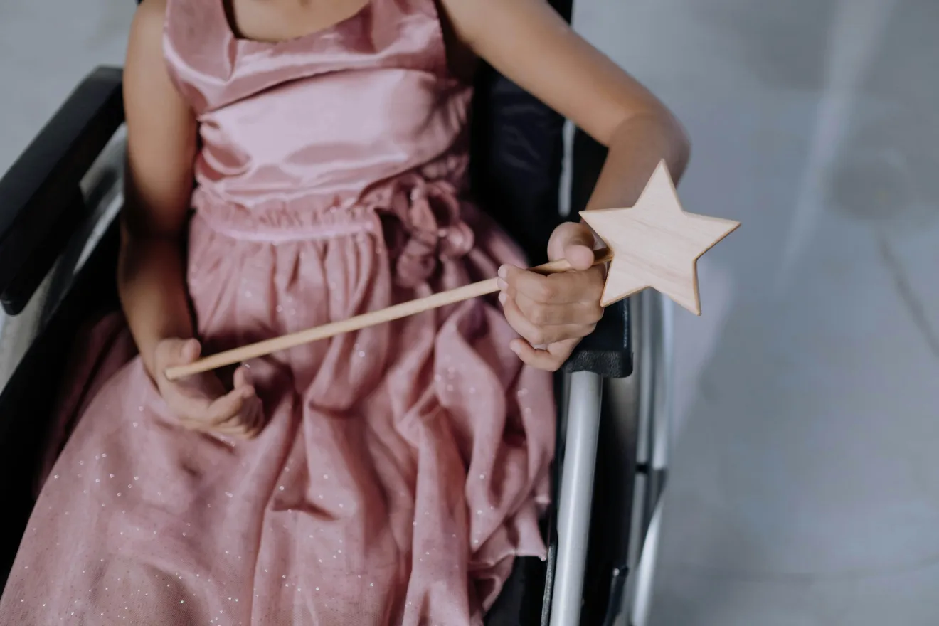 A disabled child sitting in a wheelchair, holding a toy magic wand