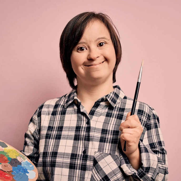 Person holding paint brush and artist's palette, smiling, on a pink background.