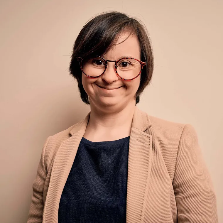 Person standing in business attire, smiling, on a beige background.